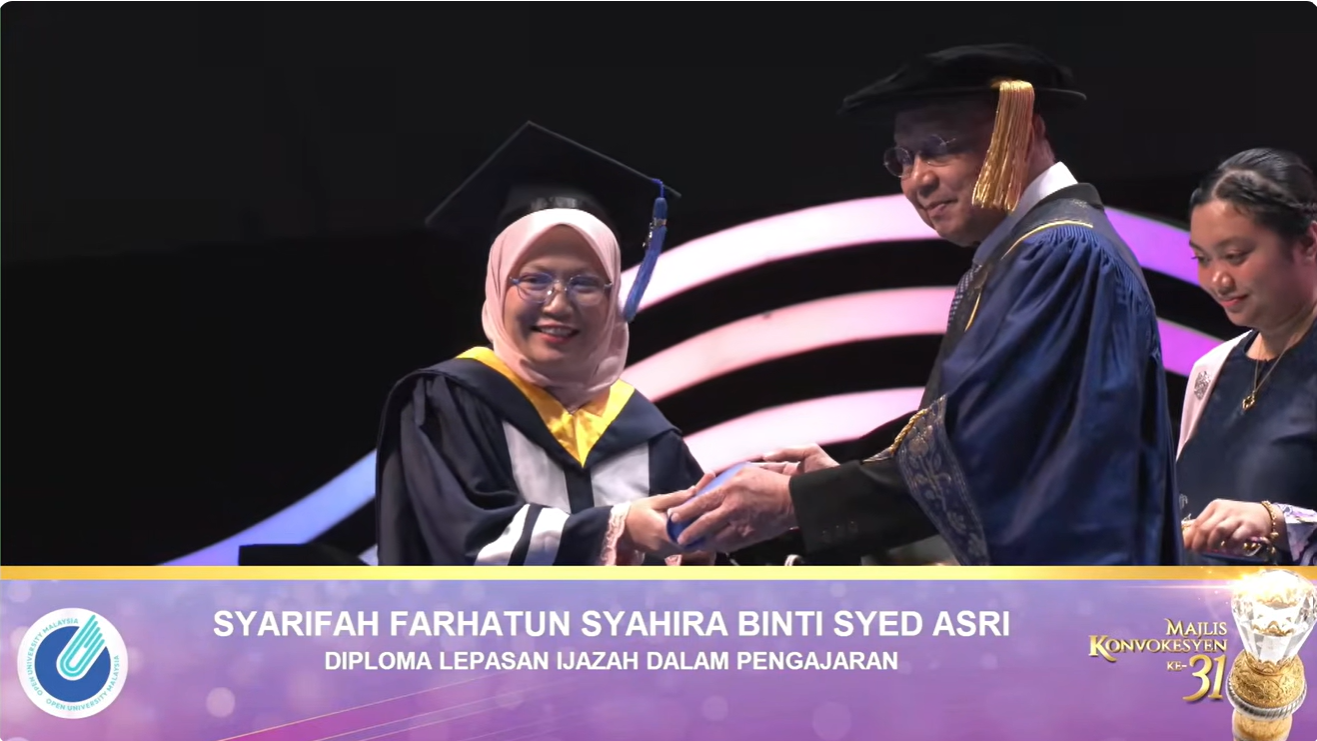 Graduan menerima skrol pada Konvokesyen OUM ke-31 dengan paparan nama dan program pengajian di bahagian bawah siaran